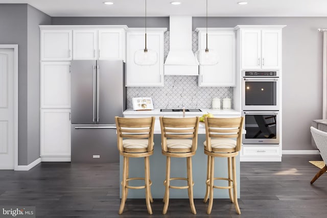 kitchen featuring premium range hood, stainless steel appliances, white cabinets, and hanging light fixtures