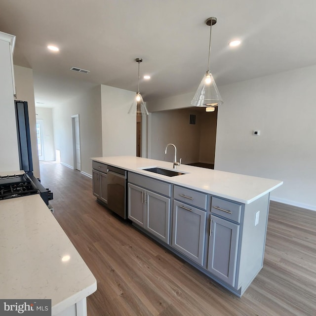 kitchen with sink, wood-type flooring, stainless steel dishwasher, and gray cabinetry