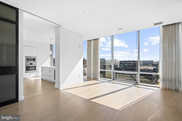 spare room with a wall of windows and light hardwood / wood-style flooring