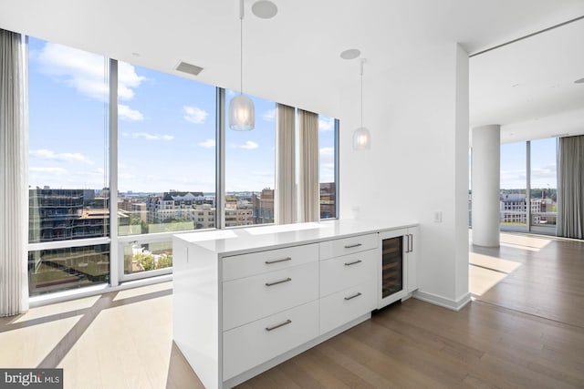 kitchen featuring expansive windows, hanging light fixtures, light wood-type flooring, white cabinetry, and beverage cooler