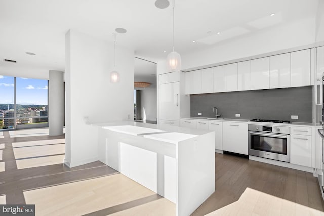 kitchen featuring backsplash, white cabinets, oven, hanging light fixtures, and kitchen peninsula