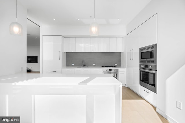 kitchen with white cabinets, decorative light fixtures, stainless steel appliances, and light hardwood / wood-style flooring