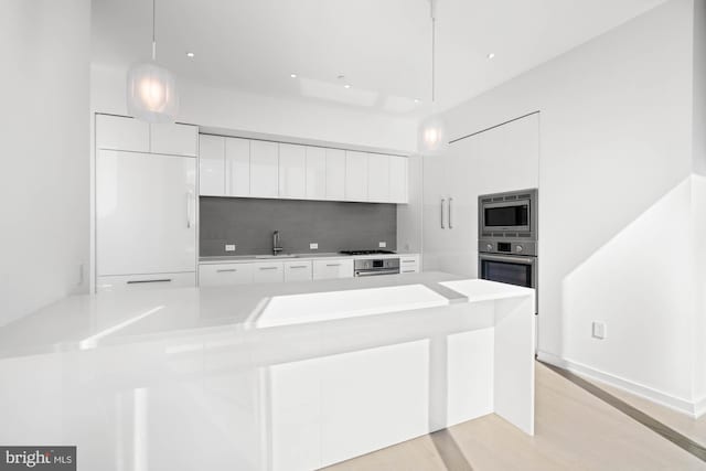 kitchen featuring sink, light hardwood / wood-style floors, decorative light fixtures, white cabinets, and appliances with stainless steel finishes