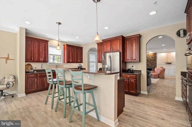 kitchen featuring a kitchen bar, appliances with stainless steel finishes, light hardwood / wood-style floors, a kitchen island, and pendant lighting