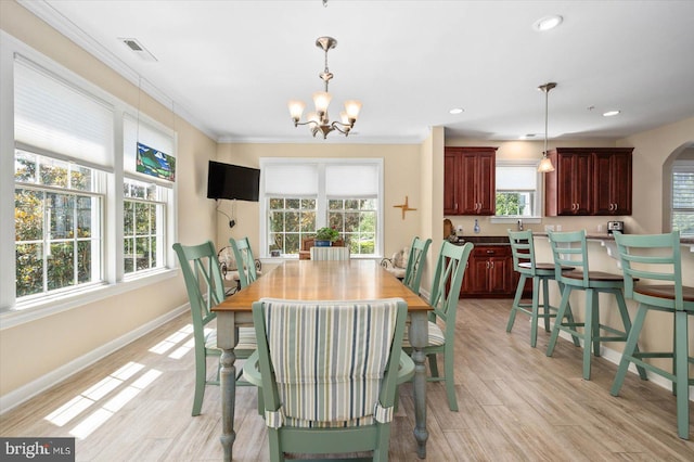 dining space with light hardwood / wood-style flooring, ornamental molding, and an inviting chandelier