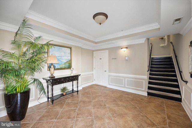 tiled foyer with a raised ceiling and ornamental molding