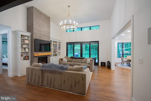 living area featuring a large fireplace, wood finished floors, a towering ceiling, and an inviting chandelier