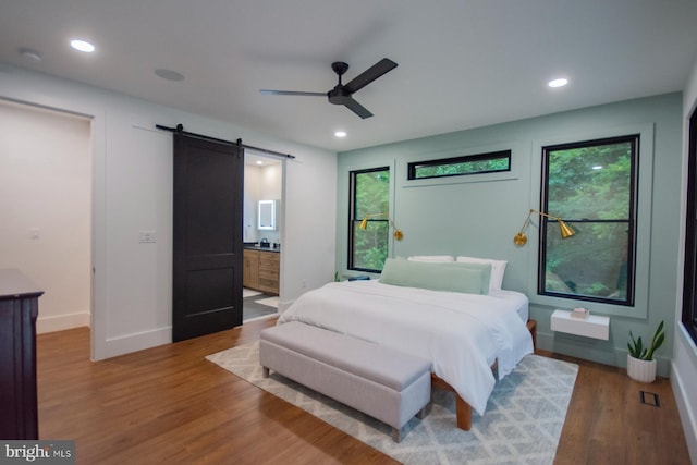 bedroom with a barn door, baseboards, connected bathroom, wood finished floors, and recessed lighting