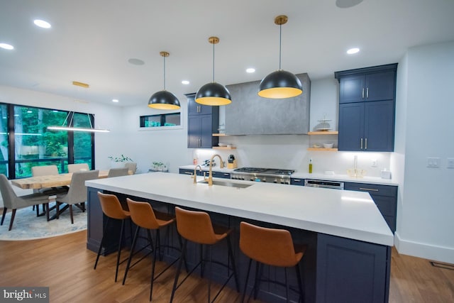 kitchen featuring a kitchen island with sink, wood finished floors, a sink, light countertops, and pendant lighting