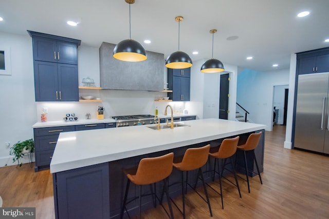 kitchen featuring light countertops, a kitchen island with sink, high quality fridge, a sink, and blue cabinets