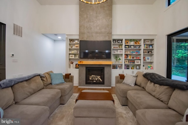 living area featuring a large fireplace, visible vents, built in features, a towering ceiling, and light wood-style floors