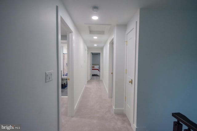 hallway with attic access, light colored carpet, and baseboards