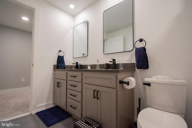 bathroom featuring double vanity, baseboards, toilet, and recessed lighting