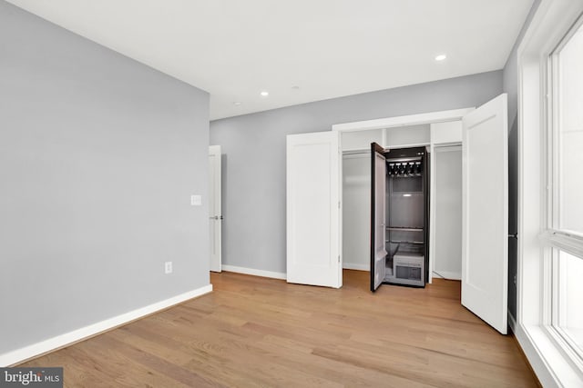 unfurnished bedroom featuring light wood-style flooring, baseboards, recessed lighting, and a closet