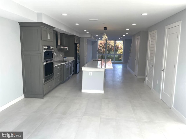 kitchen with light countertops, a chandelier, a kitchen island with sink, double oven, and freestanding refrigerator