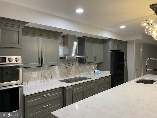 kitchen with a sink, wall chimney range hood, black appliances, light stone counters, and decorative backsplash
