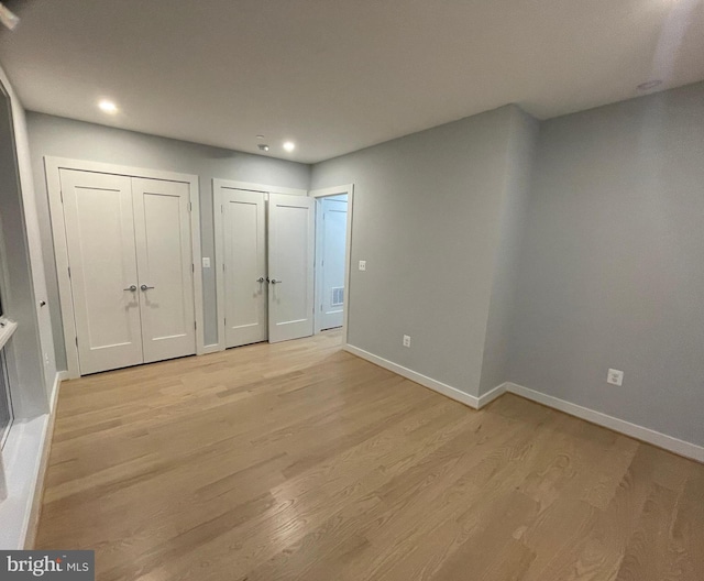 unfurnished bedroom featuring two closets, light wood-style flooring, baseboards, and recessed lighting