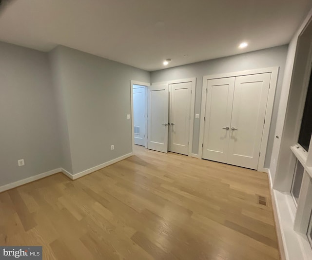 unfurnished bedroom featuring multiple closets, light wood-style flooring, baseboards, and recessed lighting