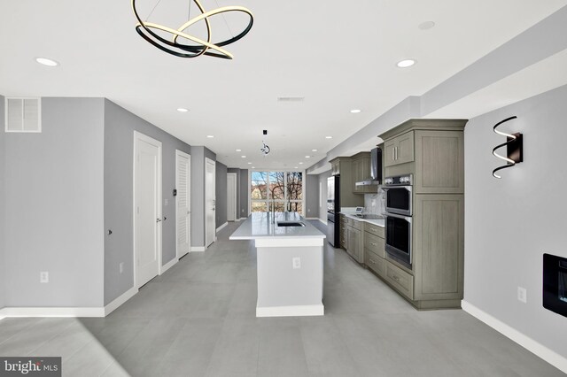 kitchen featuring stainless steel double oven, a center island with sink, light countertops, baseboards, and recessed lighting