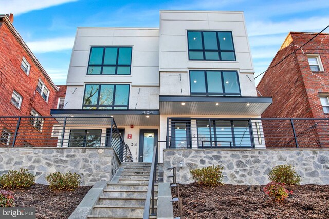 contemporary house featuring stairway, brick siding, and fence