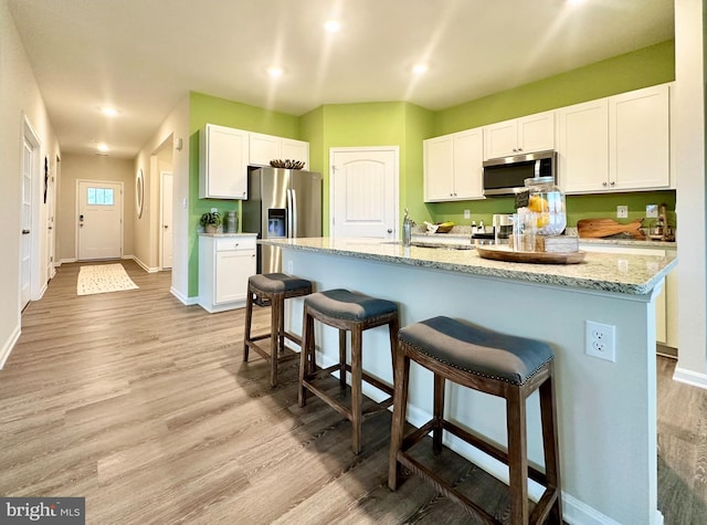 kitchen featuring white cabinetry, stainless steel appliances, a kitchen breakfast bar, light hardwood / wood-style floors, and a center island with sink