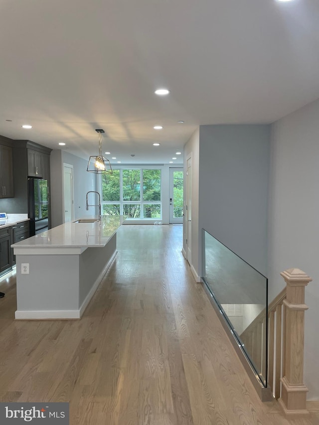 kitchen with stainless steel fridge, a center island with sink, sink, decorative light fixtures, and light wood-type flooring