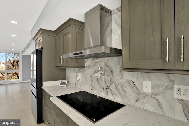 kitchen featuring wall chimney range hood, light stone counters, backsplash, light tile patterned floors, and black electric stovetop