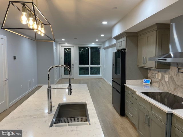 kitchen featuring black electric stovetop, decorative backsplash, hanging light fixtures, wall chimney exhaust hood, and light stone counters