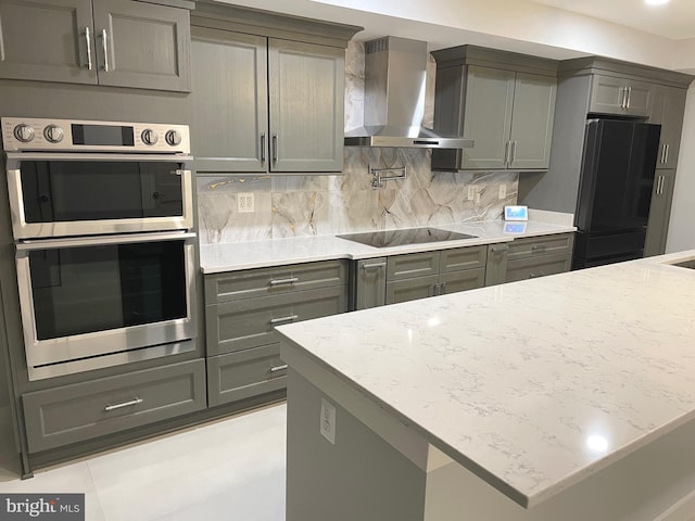 kitchen with black appliances, wall chimney exhaust hood, tasteful backsplash, light stone counters, and gray cabinetry