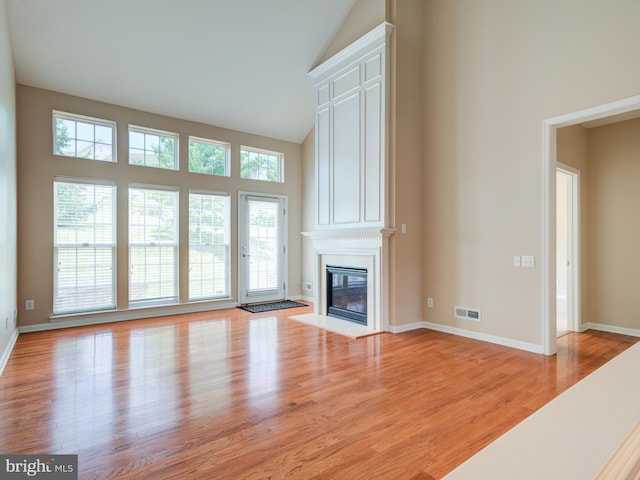 unfurnished living room featuring light hardwood / wood-style floors, a high ceiling, and a large fireplace