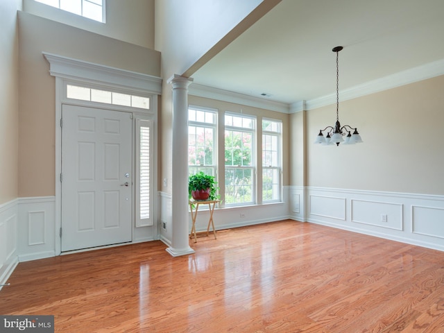 entrance foyer featuring light wood-type flooring, a notable chandelier, ornamental molding, and decorative columns