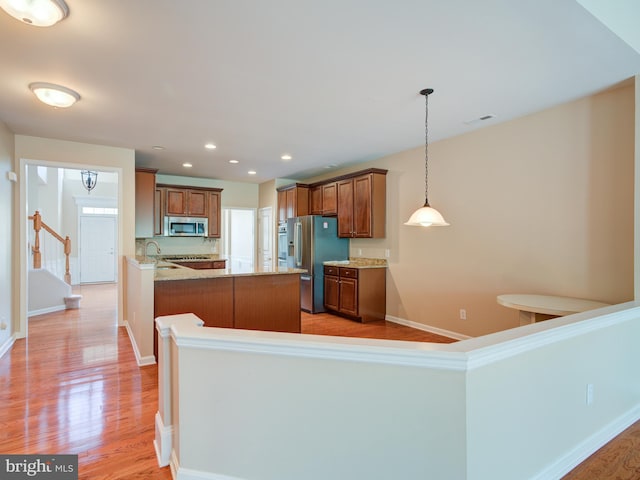 kitchen featuring pendant lighting, stainless steel appliances, light hardwood / wood-style floors, kitchen peninsula, and light stone counters