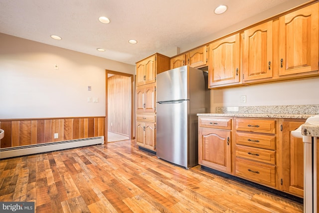 kitchen featuring a baseboard heating unit, stainless steel fridge, wooden walls, and light wood-type flooring