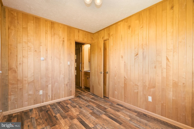 spare room featuring dark hardwood / wood-style flooring, wooden walls, and a textured ceiling