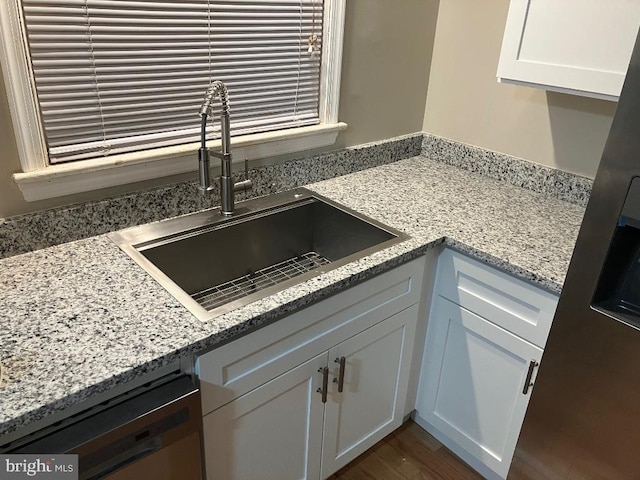 kitchen with light stone countertops, sink, white cabinets, and dishwasher