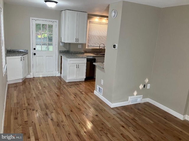 kitchen with light stone countertops, white cabinets, light wood-type flooring, and dishwasher