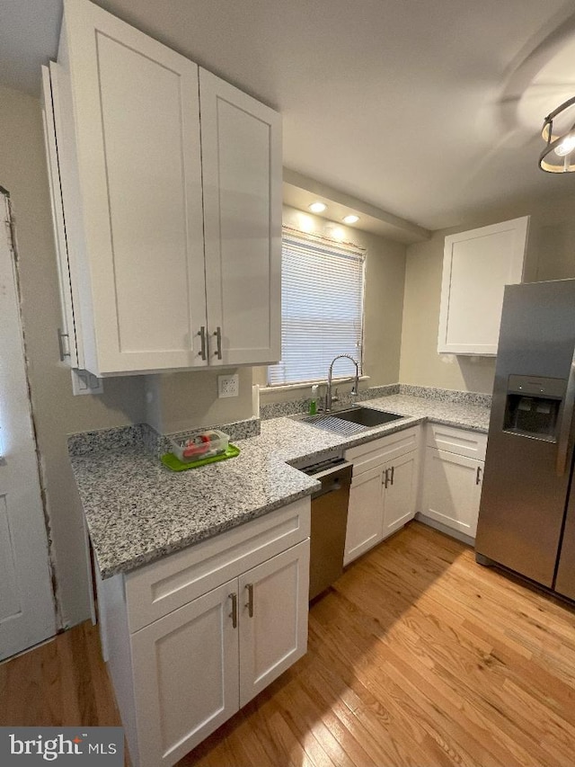 kitchen with light stone countertops, appliances with stainless steel finishes, white cabinetry, light hardwood / wood-style floors, and sink