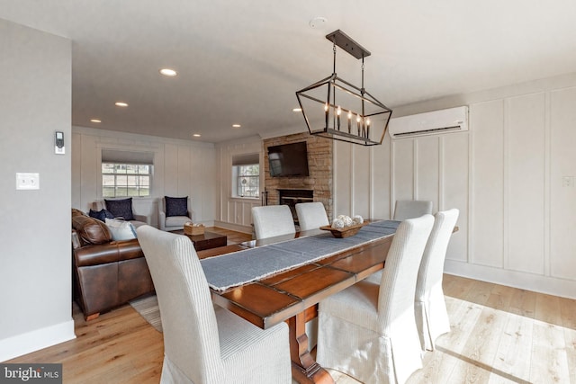 dining space with a wall mounted AC, light hardwood / wood-style floors, a notable chandelier, and a stone fireplace