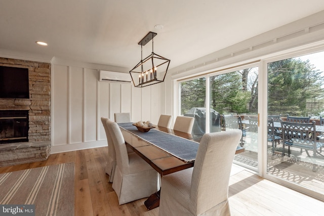 dining room featuring an AC wall unit, light hardwood / wood-style floors, a chandelier, and a stone fireplace