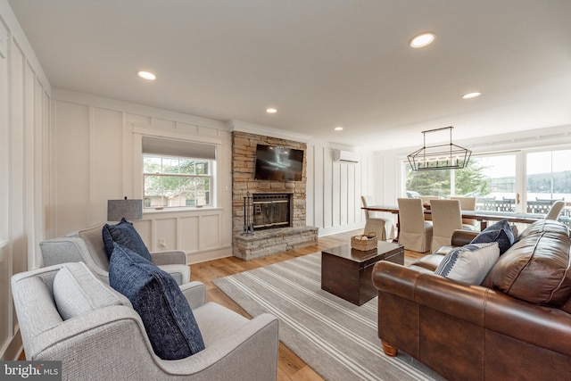 living room with a wall unit AC, light wood-type flooring, and a fireplace