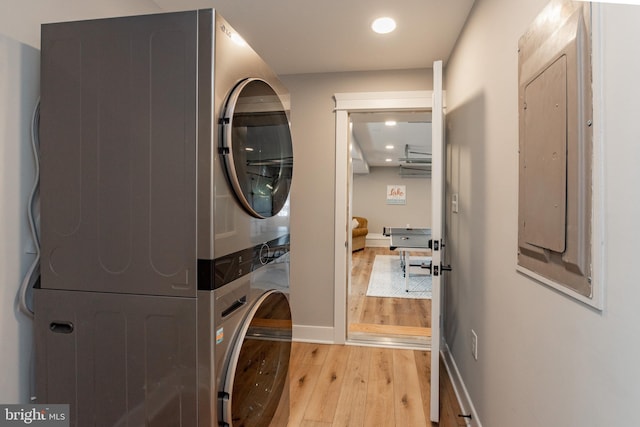 laundry room with electric panel, light hardwood / wood-style flooring, and stacked washer / dryer