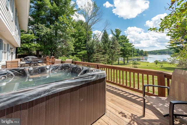 wooden terrace with a hot tub, a water view, and a lawn