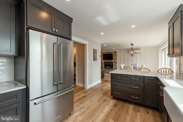 kitchen with decorative light fixtures, light wood-type flooring, backsplash, high end refrigerator, and a stone fireplace