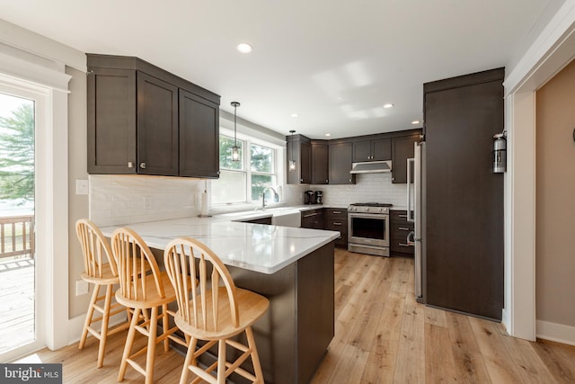 kitchen featuring light hardwood / wood-style floors, kitchen peninsula, a breakfast bar area, pendant lighting, and appliances with stainless steel finishes