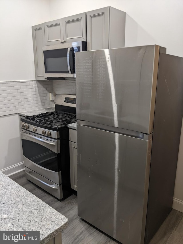 kitchen with gray cabinets, light stone counters, dark wood-type flooring, and appliances with stainless steel finishes