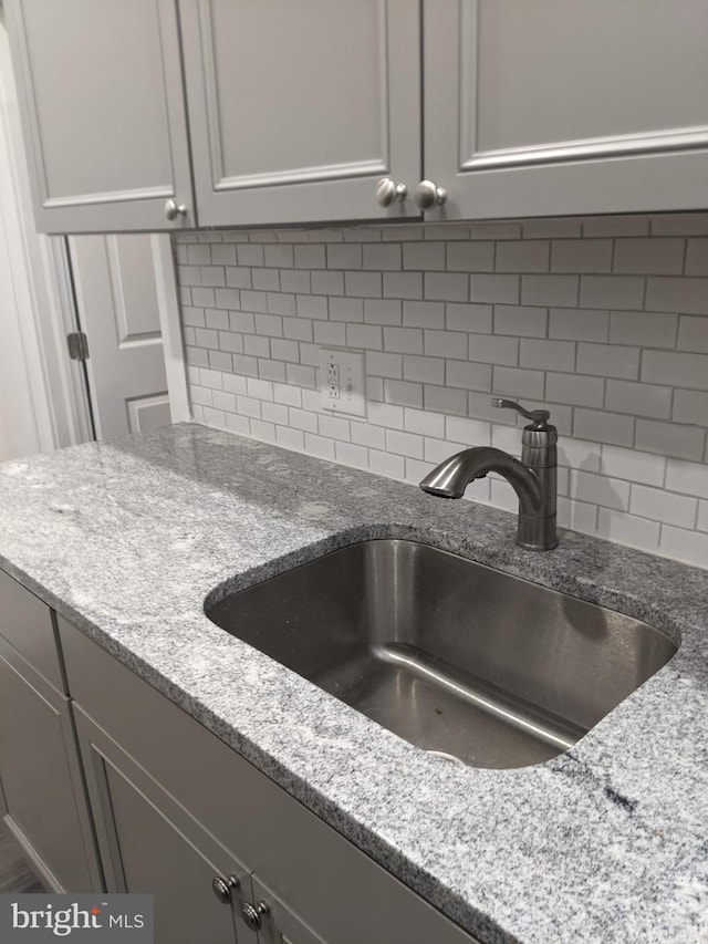 room details with backsplash, light stone countertops, and sink