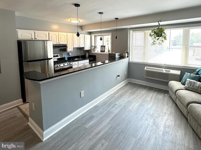 kitchen with a wall mounted air conditioner, kitchen peninsula, appliances with stainless steel finishes, decorative light fixtures, and white cabinetry