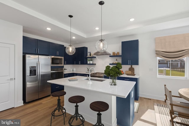 kitchen with sink, stainless steel appliances, blue cabinets, light hardwood / wood-style floors, and a breakfast bar area