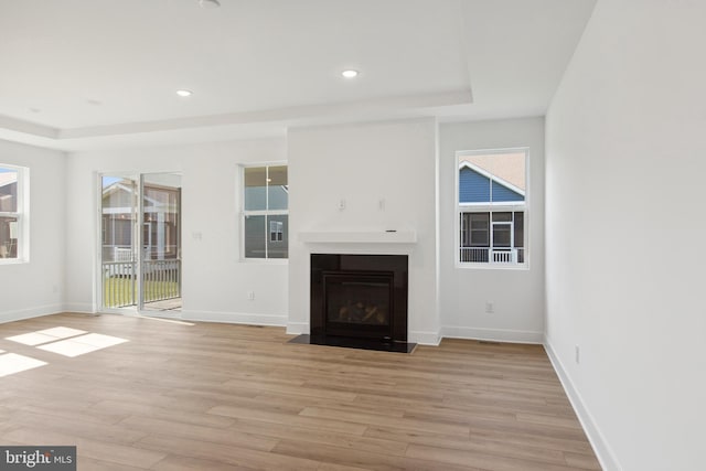 unfurnished living room featuring a tray ceiling and light hardwood / wood-style flooring