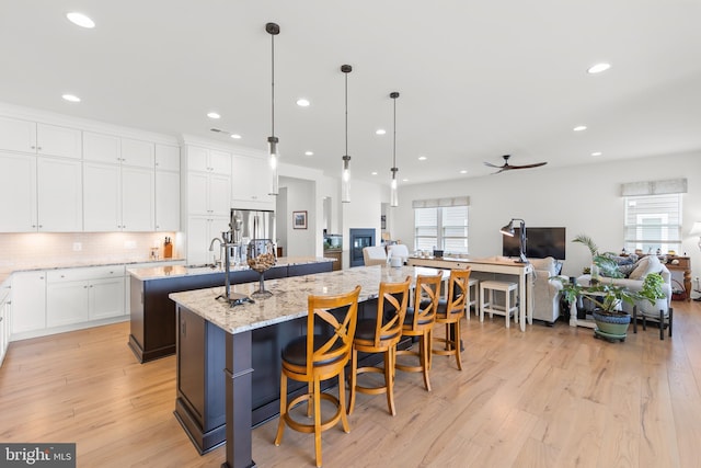 kitchen with light hardwood / wood-style flooring, sink, light stone counters, decorative backsplash, and an island with sink